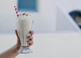 person holding clear drinking glass with white liquid