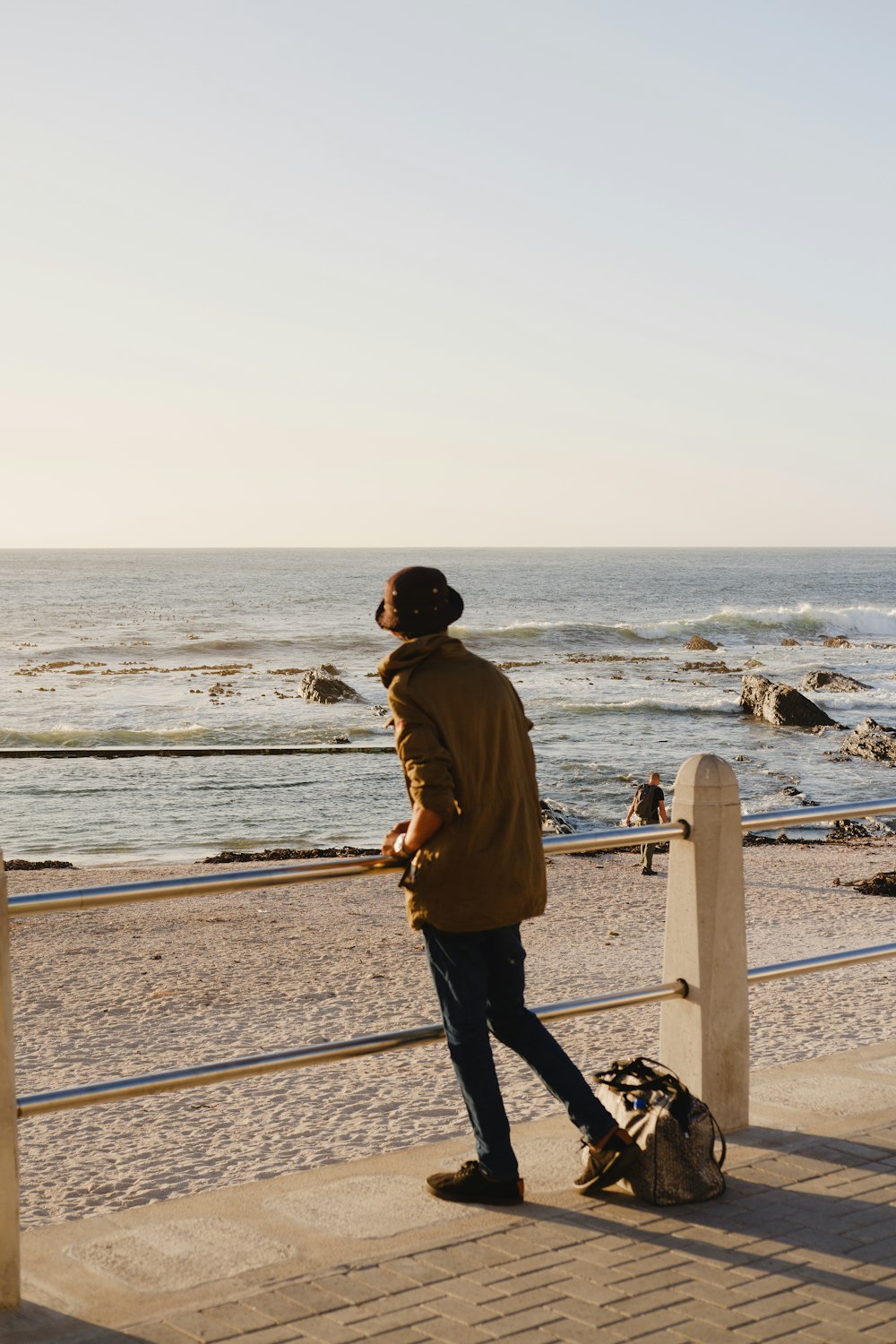 man in brown jacket and black pants standing on beach during daytime