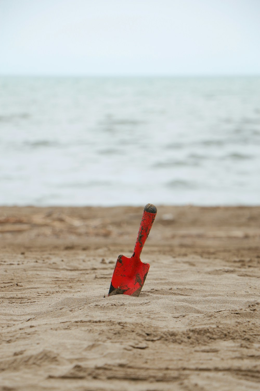 red plastic shovel on brown sand near body of water during daytime