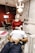 A dentist is performing a procedure on a patient reclining in a dental chair. The dentist is wearing a protective cap, mask, and gloves while using dental tools. The room features modern decor with geometric patterns on the wall, and there is a dental light overhead. Nearby, there is a table with dental instruments and a monitor on the wall.