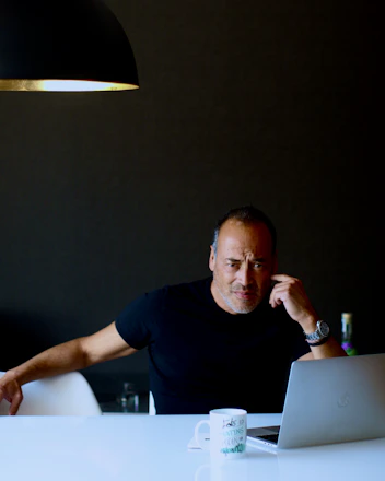 A thoughtful man reading a blog on his laptop, surrounded by notes and a cup of coffee.