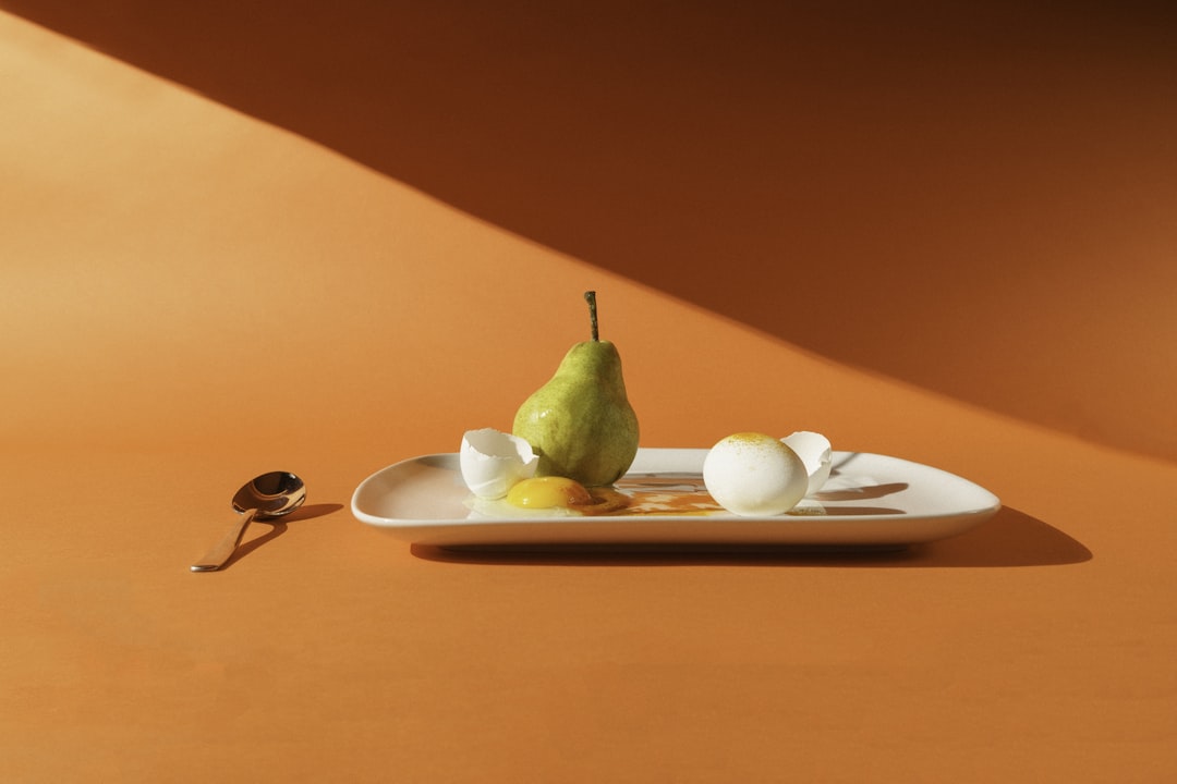 green fruit on white ceramic plate, A pear and eggs with a simple orange background