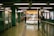A busy underground station with people walking and signs displayed above. The station is brightly lit with advertisements along the walls and a service center booth in the middle.
