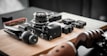 A collection of camera equipment and accessories is arranged on a wooden surface. Prominent items include a camera with a lens attached, a small tripod, and several other small electronic devices. The setting appears organized and focused, highlighting the tools for photography.