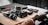 A collection of camera equipment and accessories is arranged on a wooden surface. Prominent items include a camera with a lens attached, a small tripod, and several other small electronic devices. The setting appears organized and focused, highlighting the tools for photography.