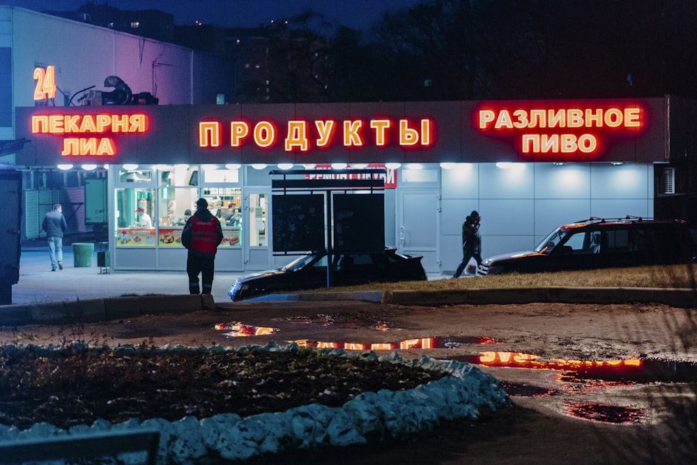 man in black jacket and black pants standing near red and white UNKs store during