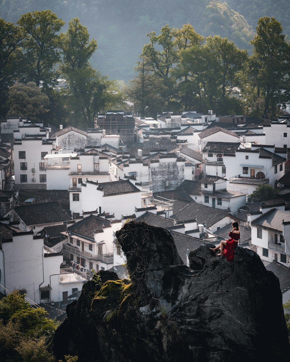 Person in roter Jacke, die tagsüber auf einem Felsen in der Nähe eines Gewässers steht