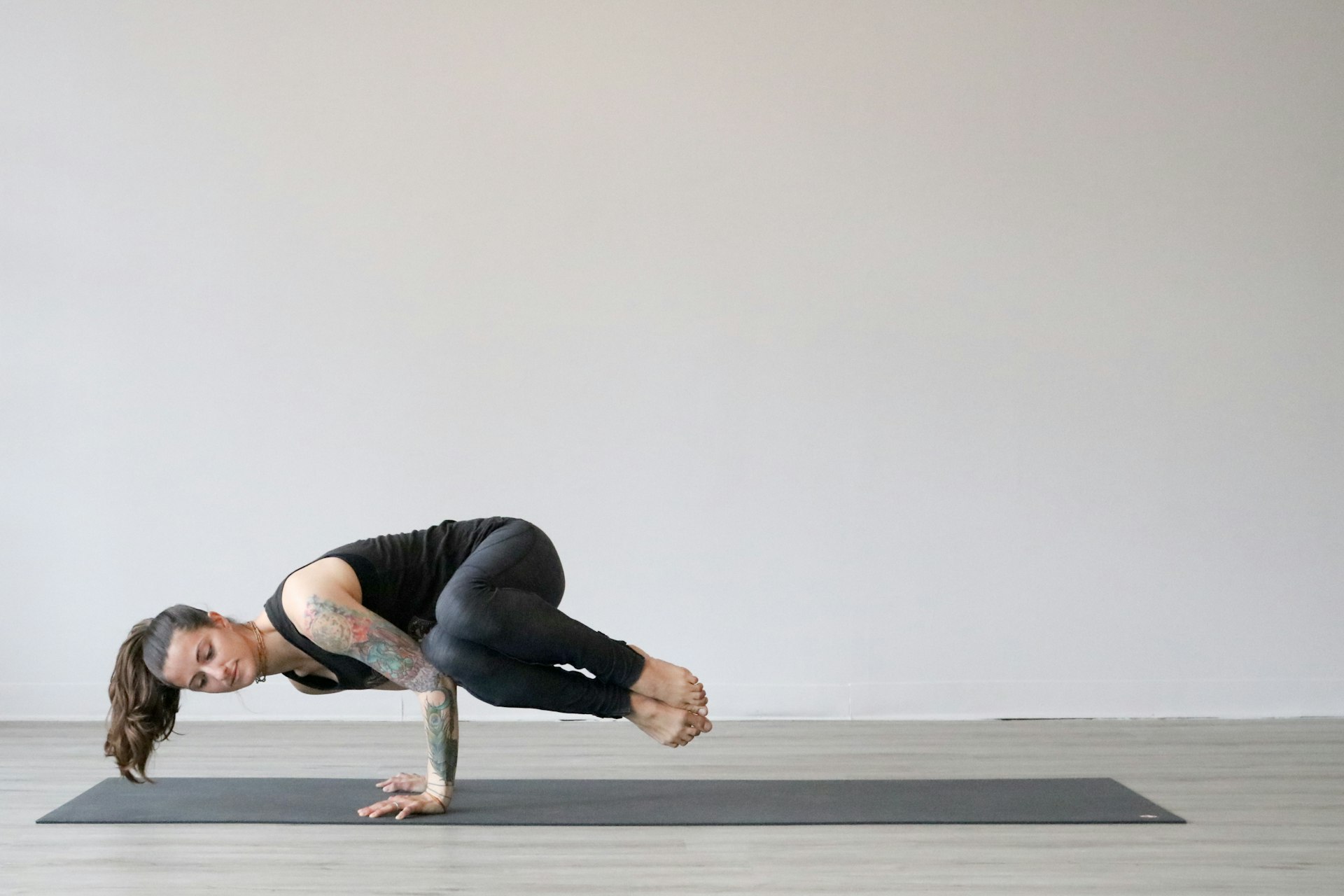 Woman in side crane pose, both knees stacked on one bent arm with her feet together