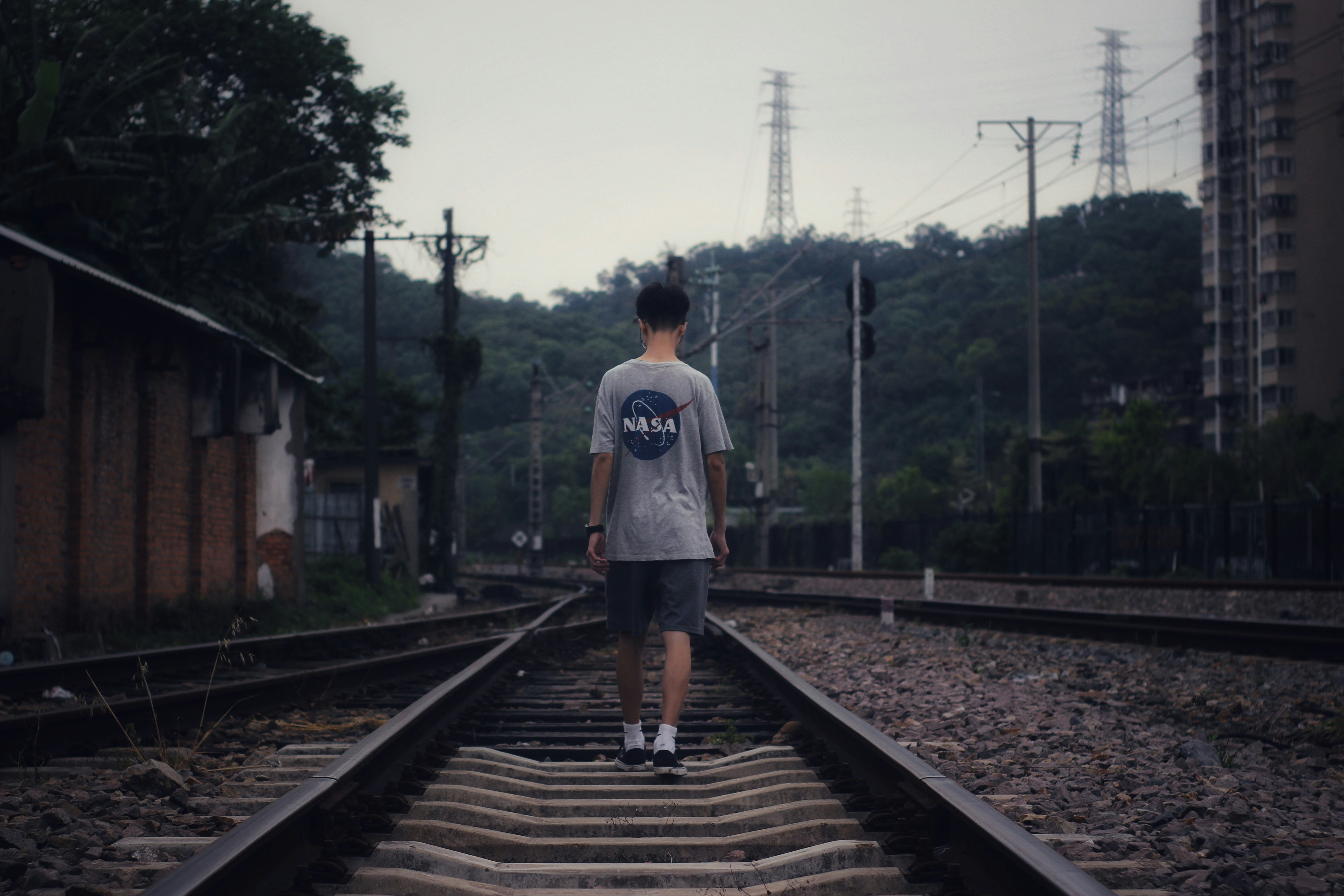 man in white t-shirt standing on train rail during daytime