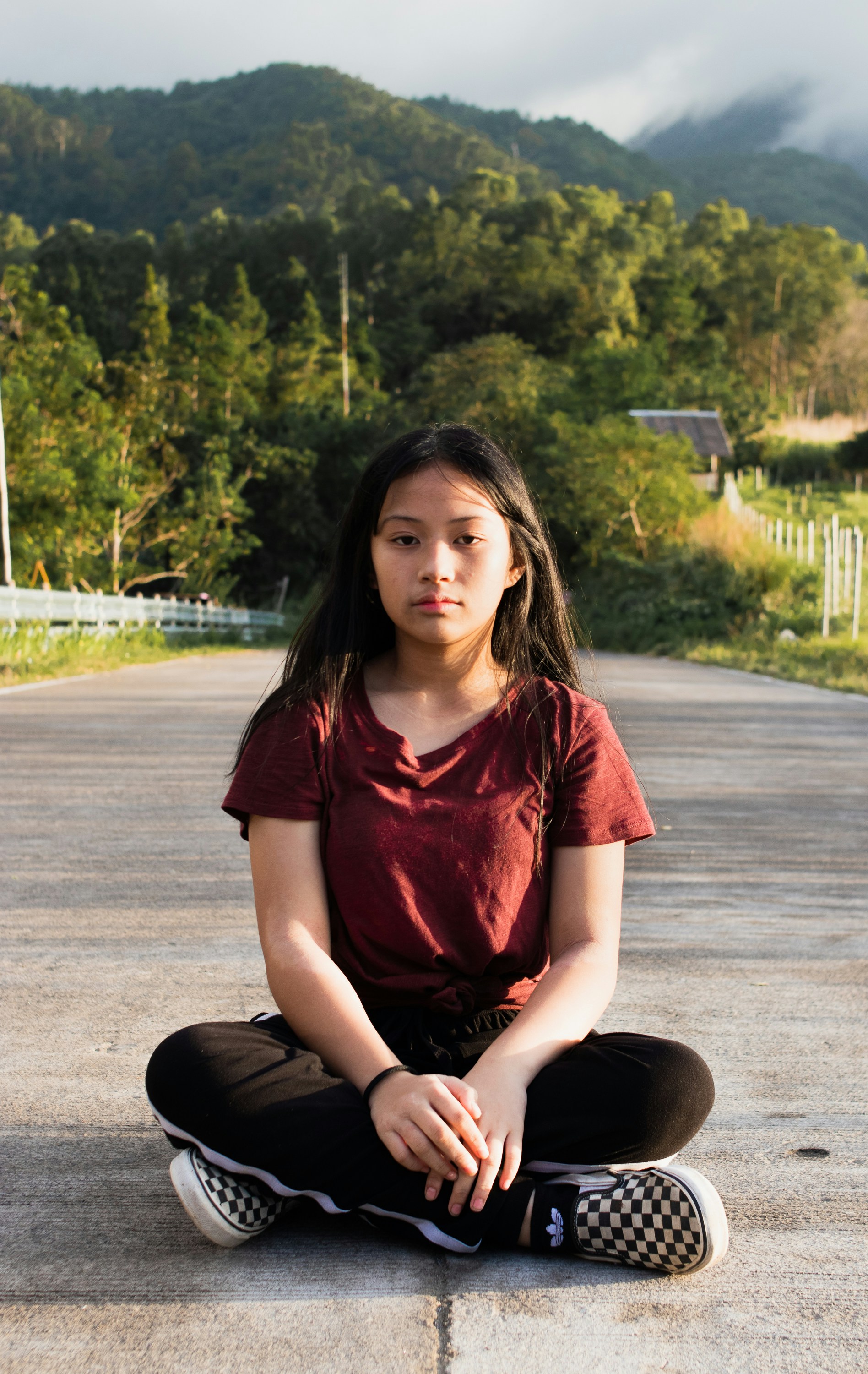 Woman in red crew neck t-shirt and black pants sitting on gray concrete road during daytime