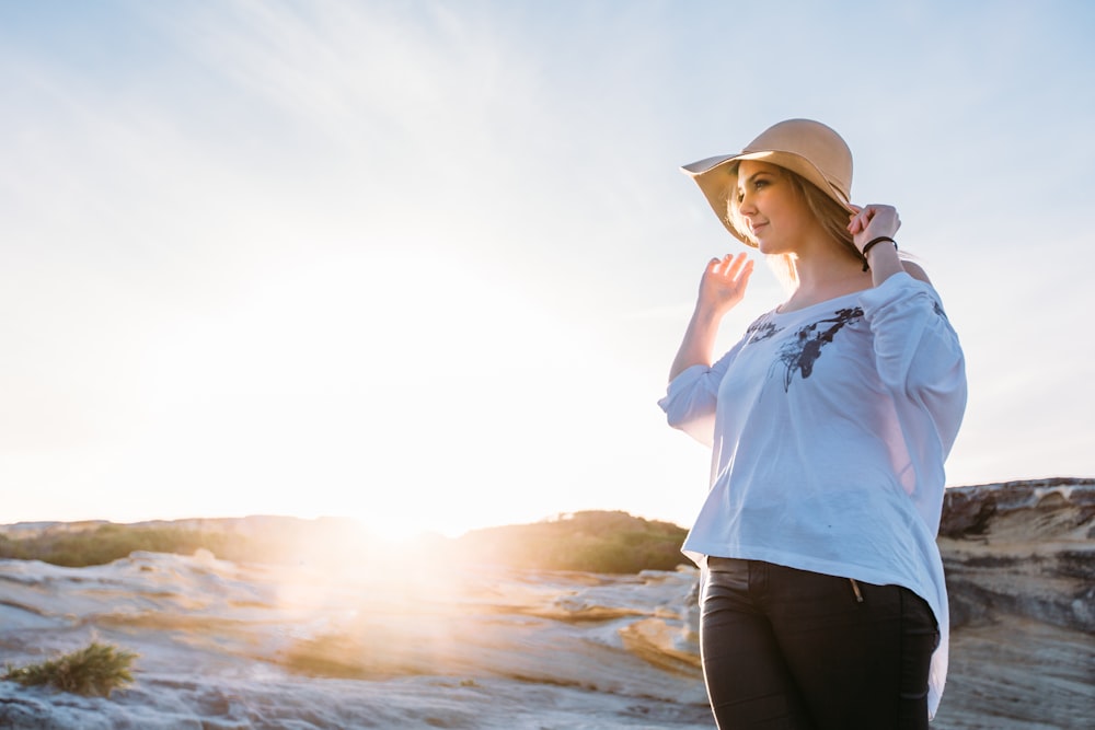 woman in blue shirt and black pants wearing brown fedora hat standing on seashore during daytime