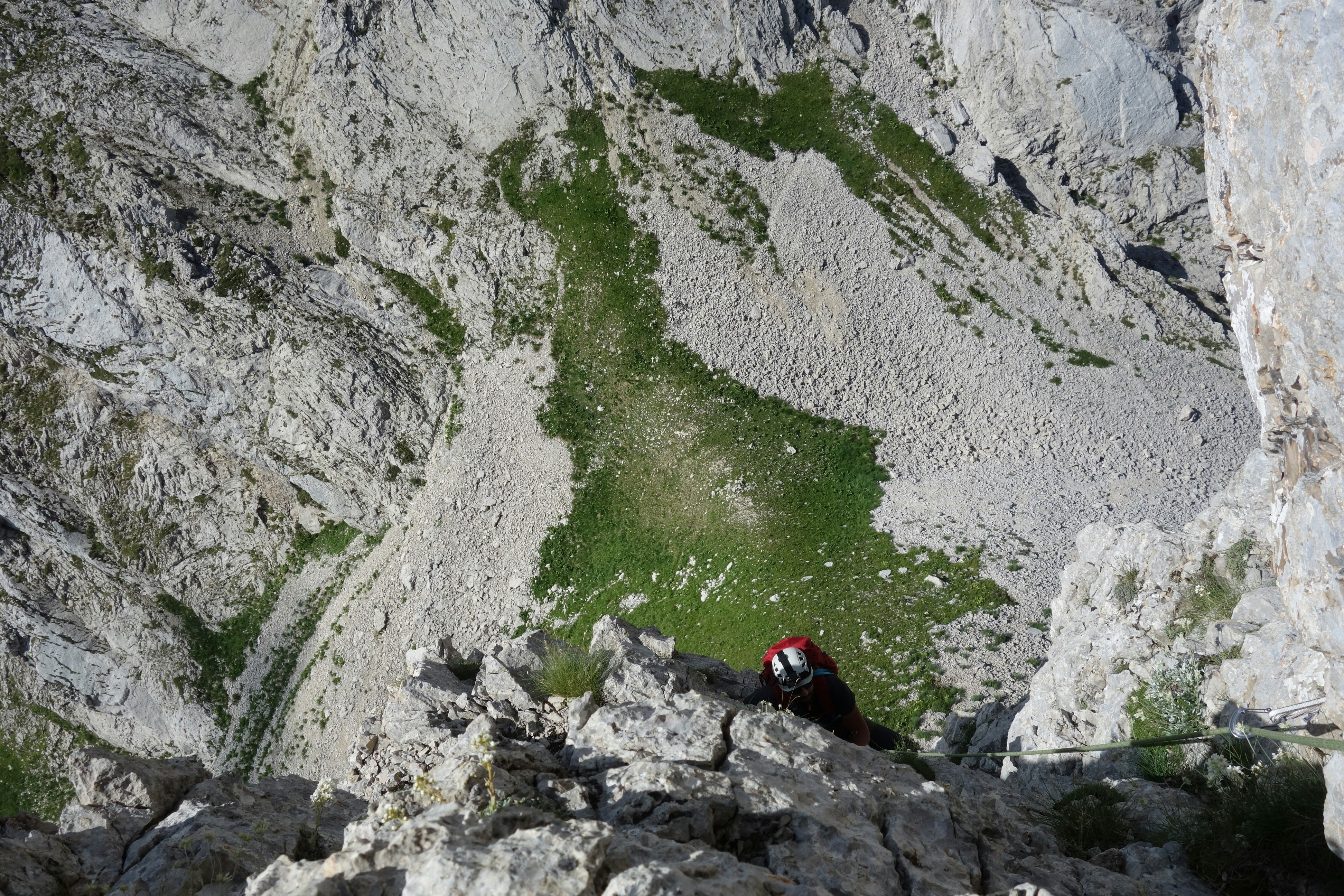 person in red jacket sitting on rock near body of water during daytime