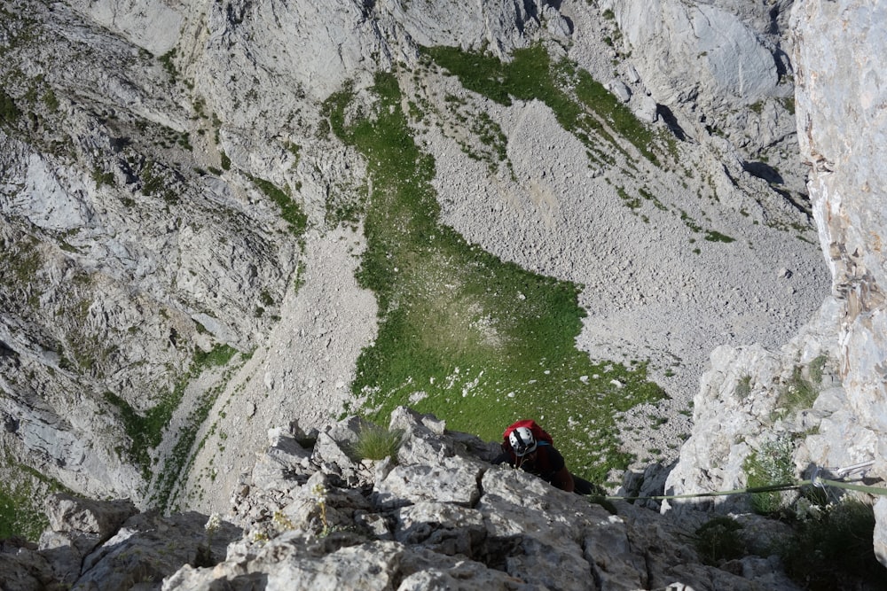 person in red jacket sitting on rock near body of water during daytime