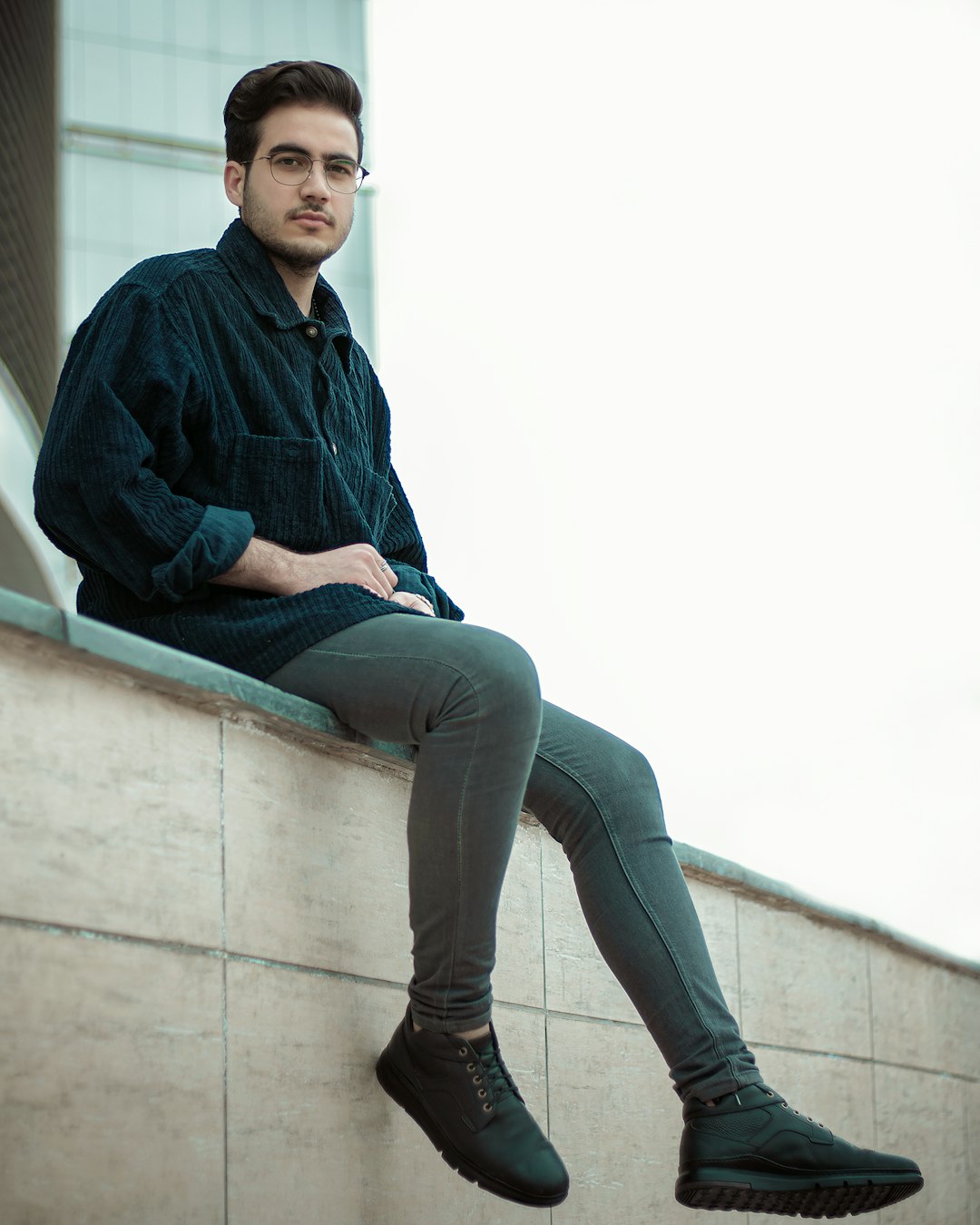 man in blue and black plaid dress shirt and gray denim jeans sitting on white concrete