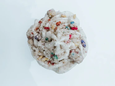 A close-up of a moist, frosted cupcake topped with a swirl of creamy vanilla icing and a sprinkle of colorful sugar.