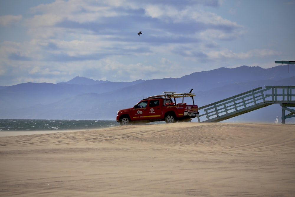 a red truck driving on top of a sandy beach