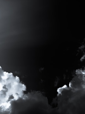 Dark, moody sky with heavy, thick clouds partially illuminated by light. The contrast between the bright clouds and the deep, dark sky creates a dramatic effect.