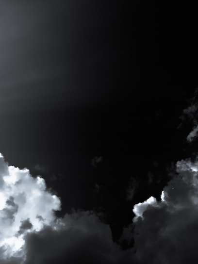 Dark, moody sky with heavy, thick clouds partially illuminated by light. The contrast between the bright clouds and the deep, dark sky creates a dramatic effect.