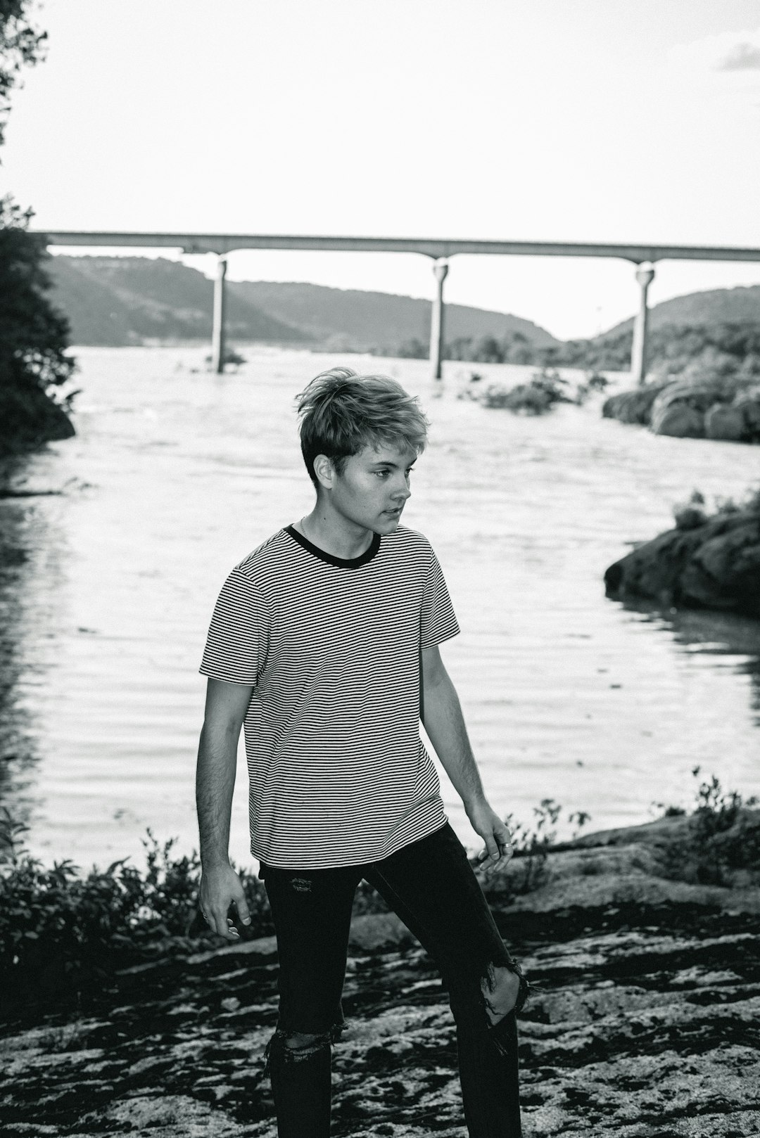 grayscale photo of man in striped shirt standing near body of water