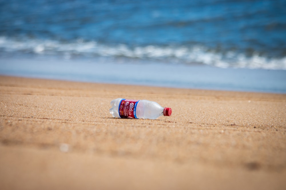 Bouteille en plastique blanche et bleue sur le rivage de la plage pendant la journée