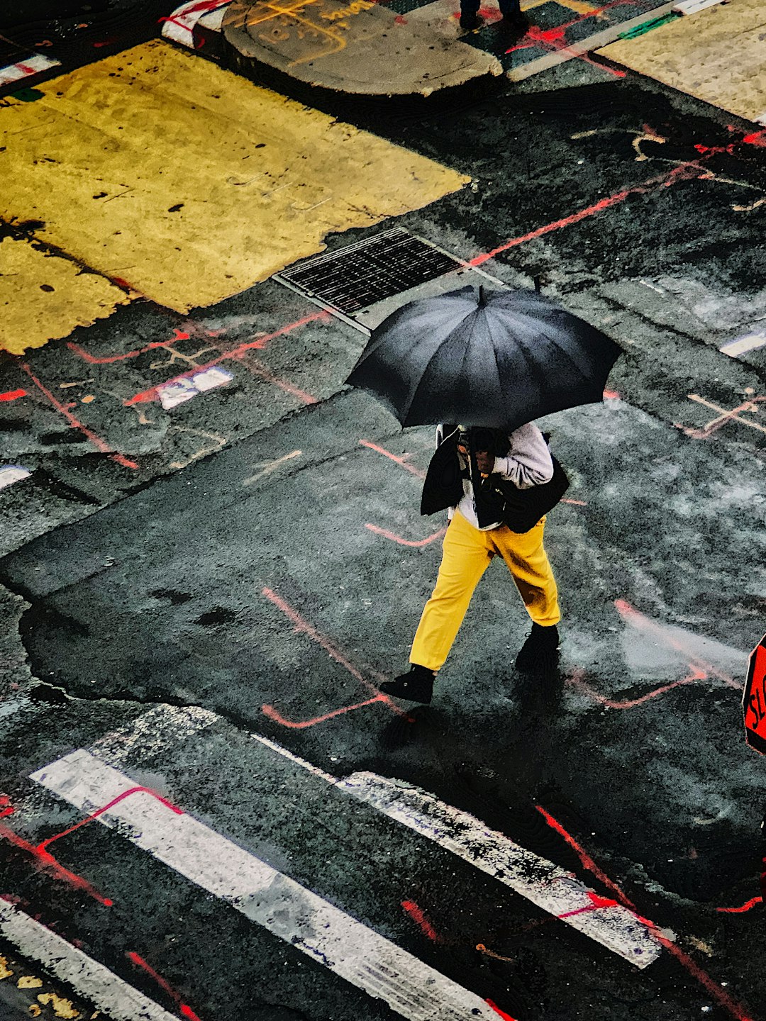 person in yellow pants and yellow jacket holding umbrella walking on wet road