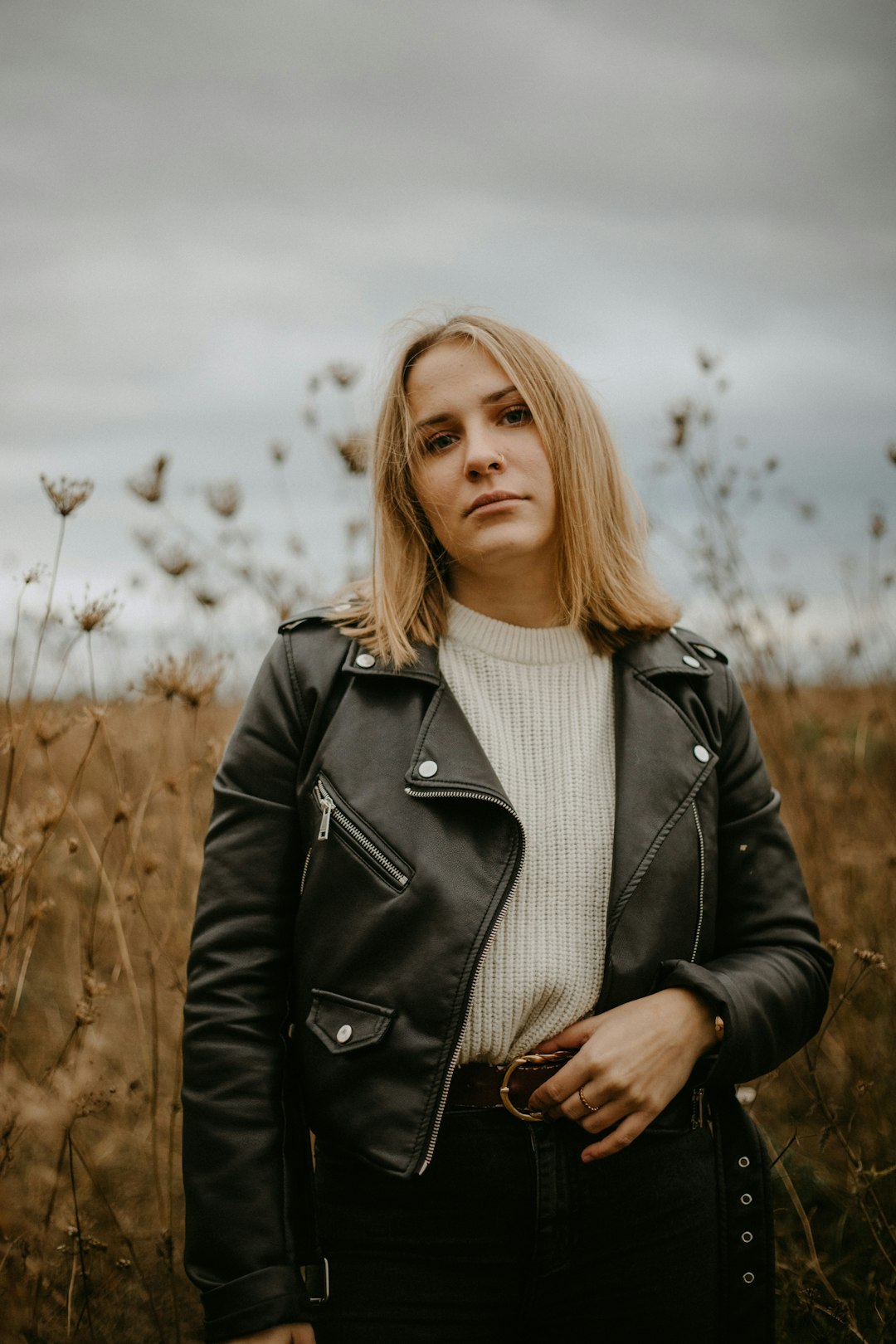 woman in black leather jacket standing on brown grass field during daytime