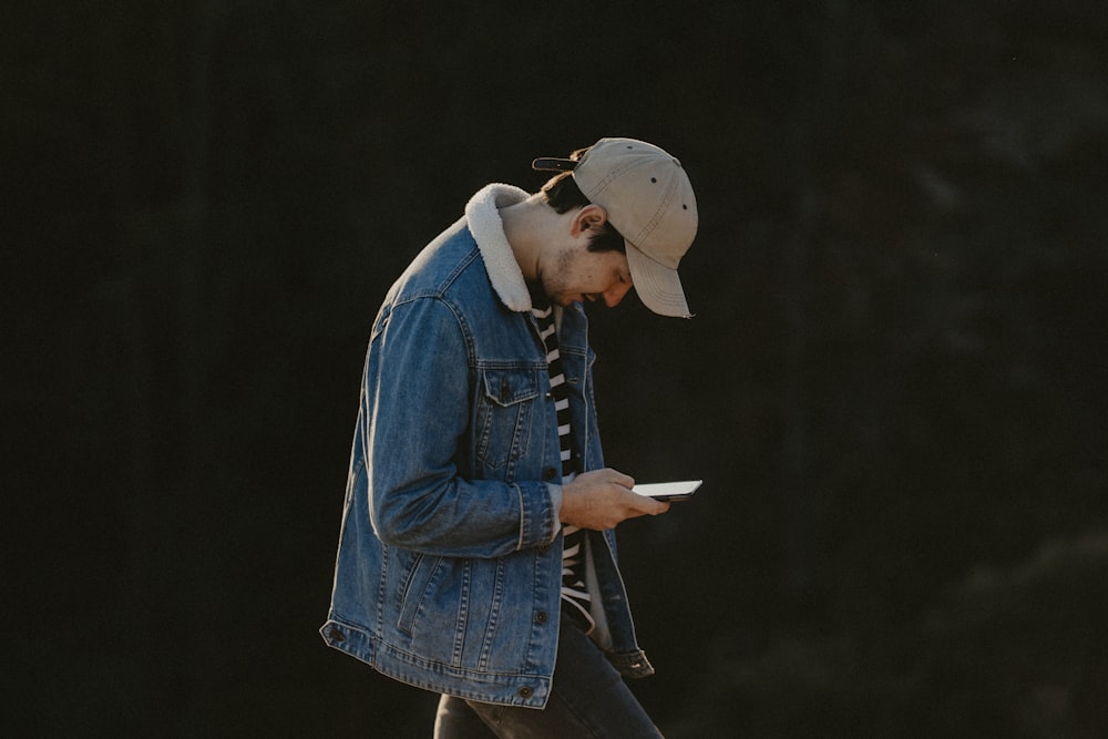 woman in blue denim jacket and brown hat holding white book