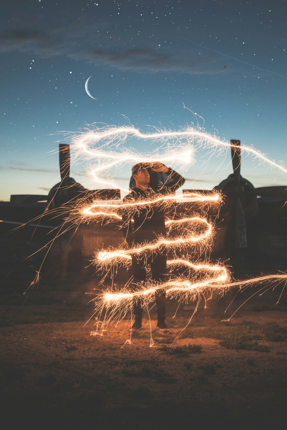 man in black jacket sitting on brown rock under blue sky with stars during night time