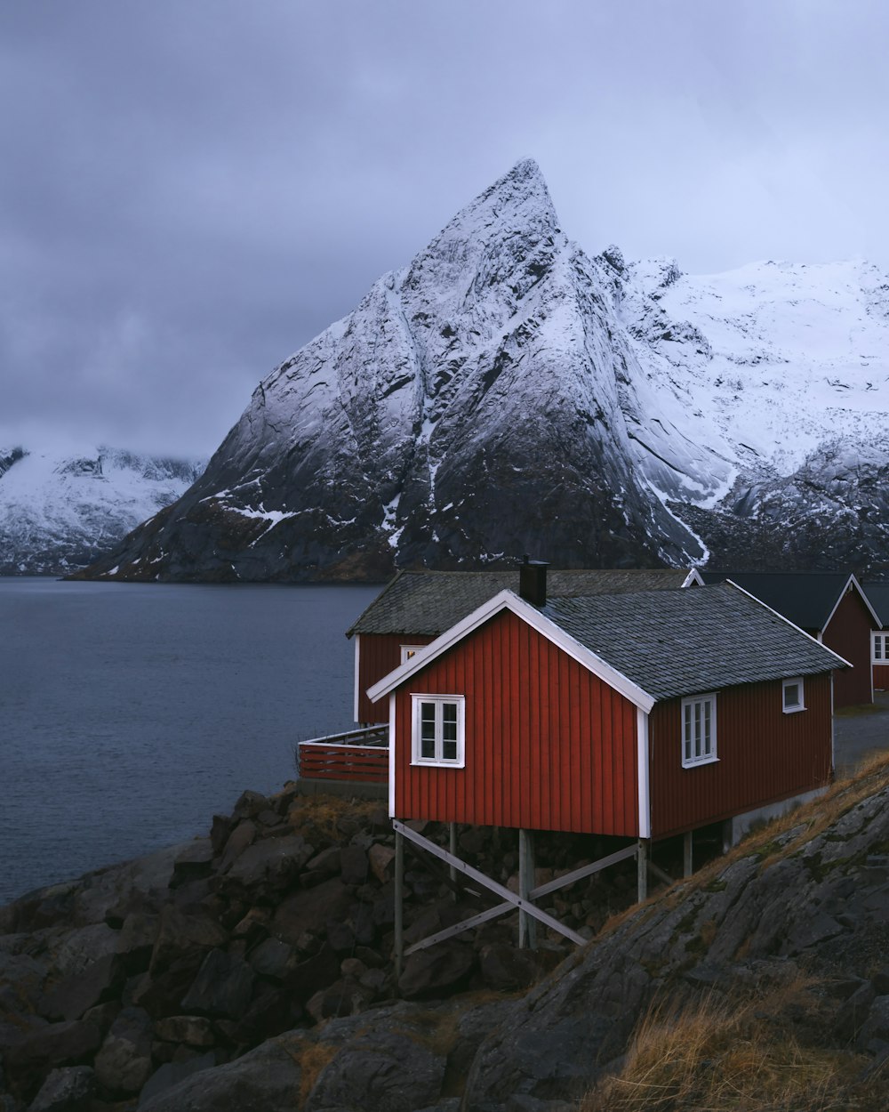 casa di legno rossa e bianca vicino allo specchio d'acqua e alla montagna coperta di neve durante il giorno