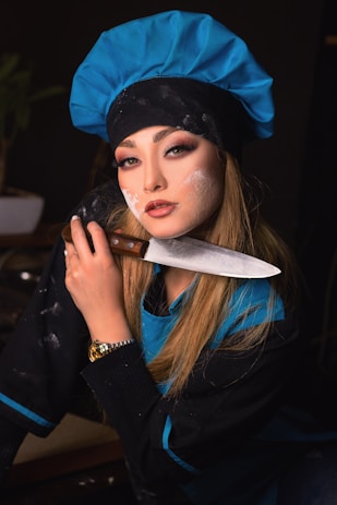 A friendly culinary instructor smiling while holding a chef's knife in a professional kitchen setting.