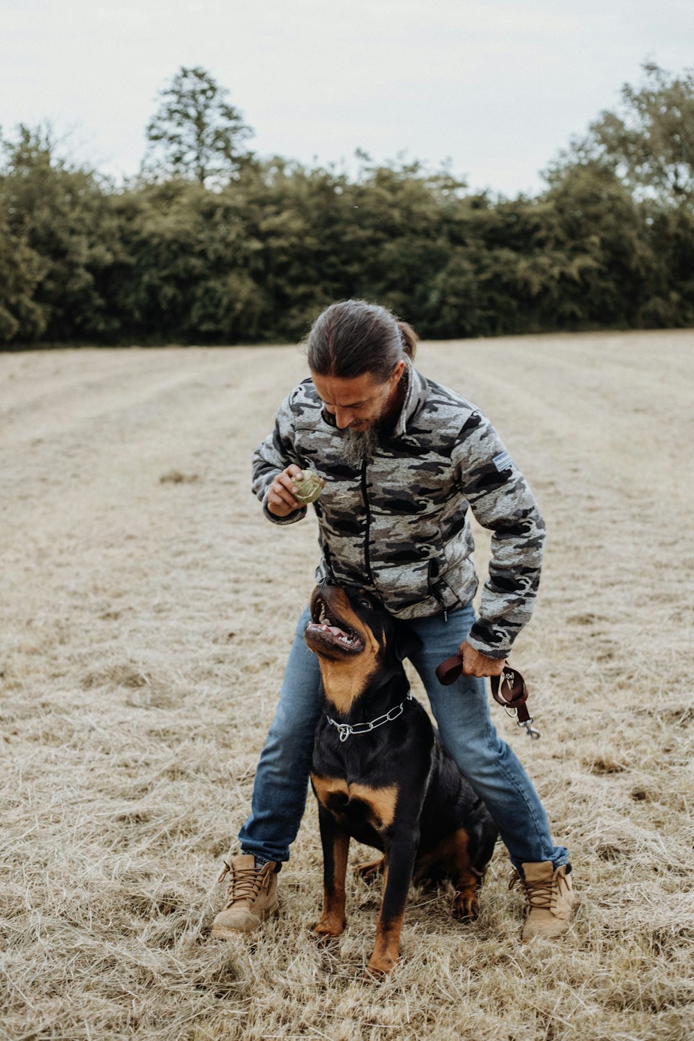 boy in camouflage jacket and blue denim jeans holding black and brown short coated dog