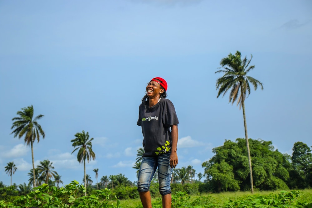 man in black crew neck t-shirt and blue denim shorts standing near green palm tree