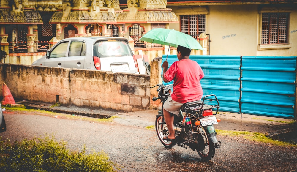 man in orange long sleeve shirt riding motorcycle with umbrella