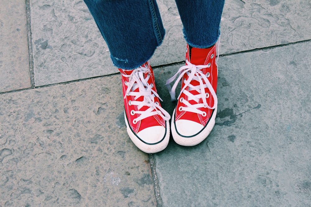 person in blue denim jeans and red and white converse all star high top sneakers