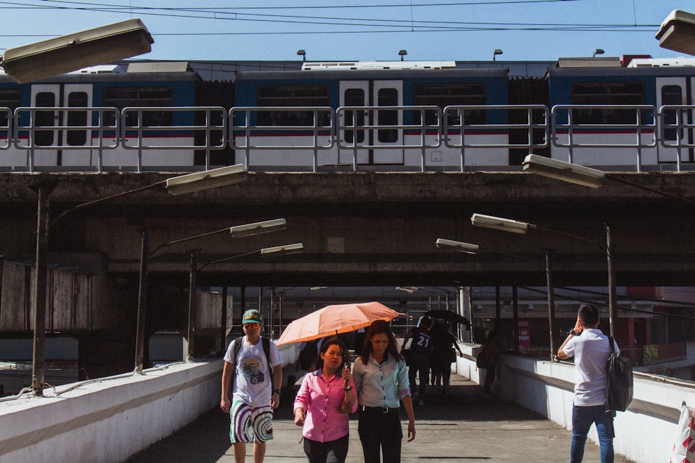 2 women and man holding umbrella walking on sidewalk during daytime