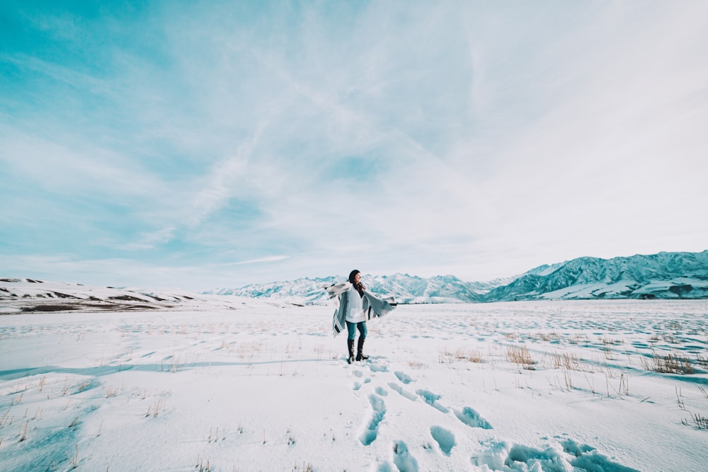 Frau in weißer Jacke geht tagsüber auf schneebedecktem Feld spazieren