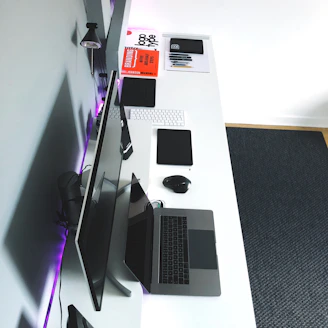 A minimalist workspace with clean white surfaces, a sleek laptop, and a stack of children’s books beside financial reports.