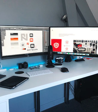 A sleek, modern workspace with dual monitors displaying dynamic digital designs and futuristic interfaces.
