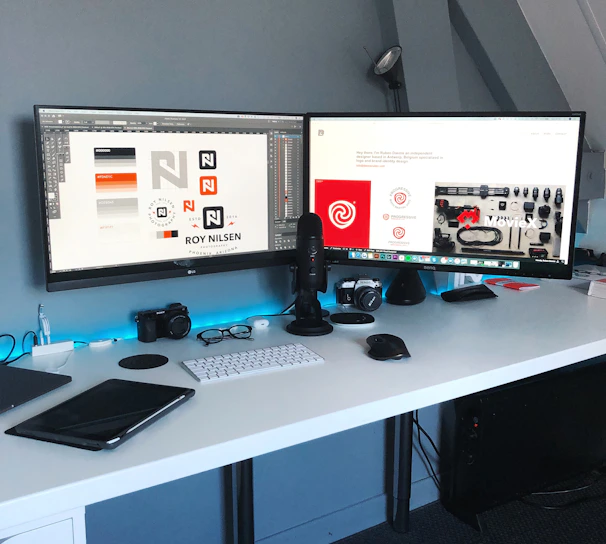 A sleek, modern workspace with dual monitors displaying dynamic digital designs and futuristic interfaces.