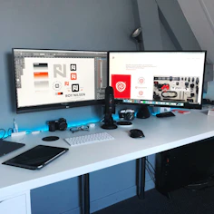 A modern workspace setup with dual monitors displaying AWS and Azure dashboards under soft ambient lighting.