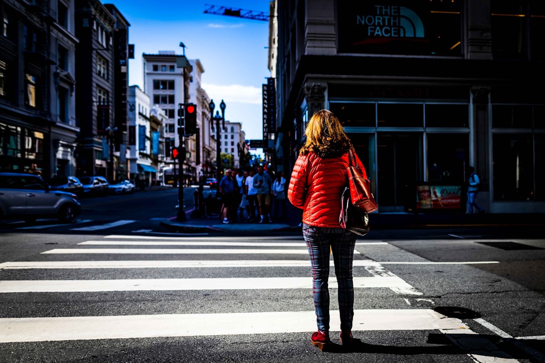 woman in red jacket and blue denim jeans standing on pedestrian lane during daytime