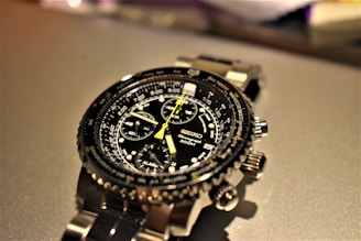 A detailed wristwatch with a black dial featuring multiple subdials and a yellow second hand. The watch has a stainless steel strap and various markings and labels, including '200M' and 'Seiko'. The background is out of focus, drawing attention to the watch.