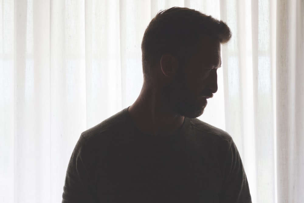 man in gray crew neck shirt standing near white window curtain