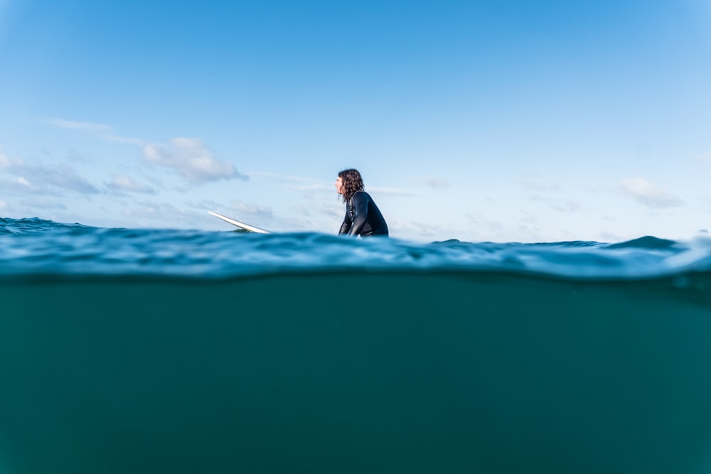 man in black jacket sitting on blue surfboard during daytime