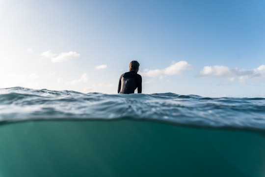 woman in black shirt sitting on sea water during daytime in Te Arai New Zealand