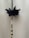A decorative string made of black beads is adorned with a black fabric flower and interspersed with metallic gold and clear beads. The background is a plain beige surface.