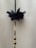 A decorative string made of black beads is adorned with a black fabric flower and interspersed with metallic gold and clear beads. The background is a plain beige surface.