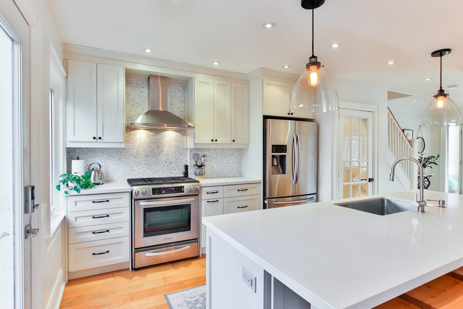 Bright white kitchen with a large island, stainless steel appliances and pendant lighting