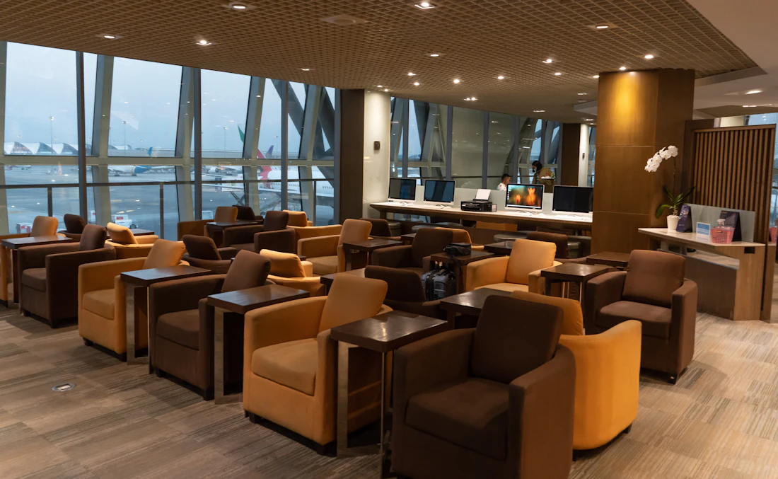 Armchairs and side tables in a SkyLounge Premium departure lounge facing floor-to-ceiling apron windows