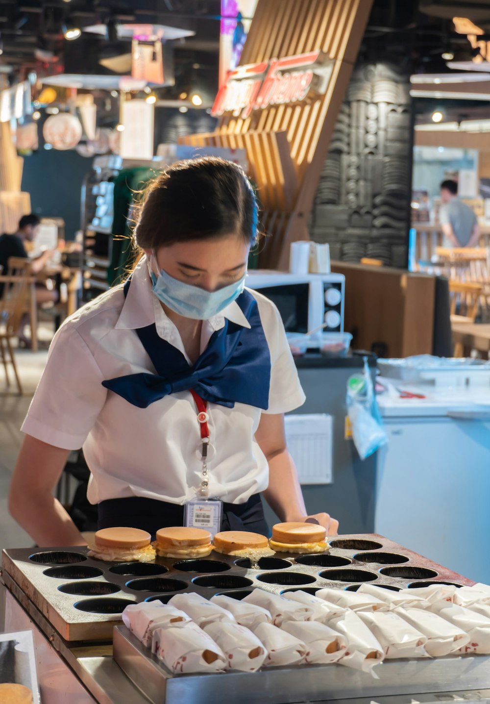 woman in white and blue school uniform standing in front of table with cupcakes